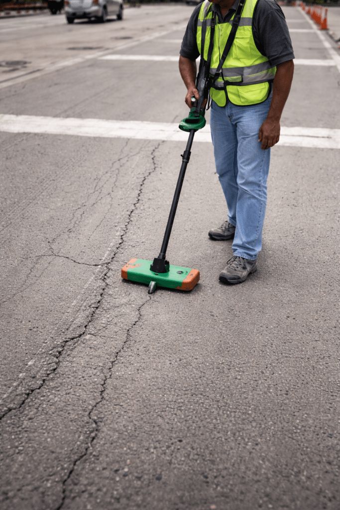 Technician performing pavement surface testing using field equipment on asphalt road
